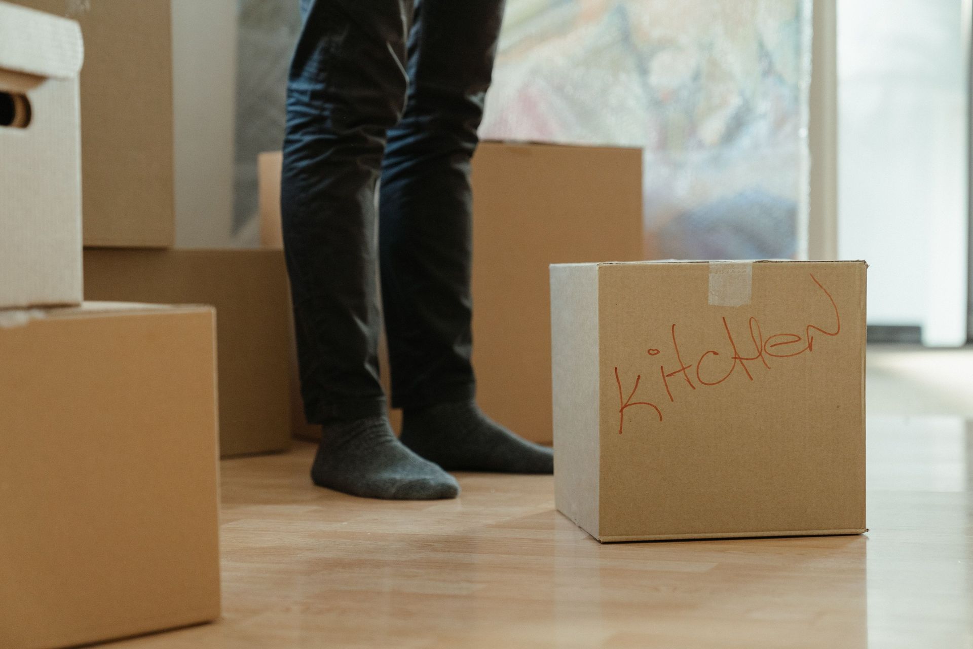 A person standing in a room surrounded by moving boxes labeled for the kitchen.